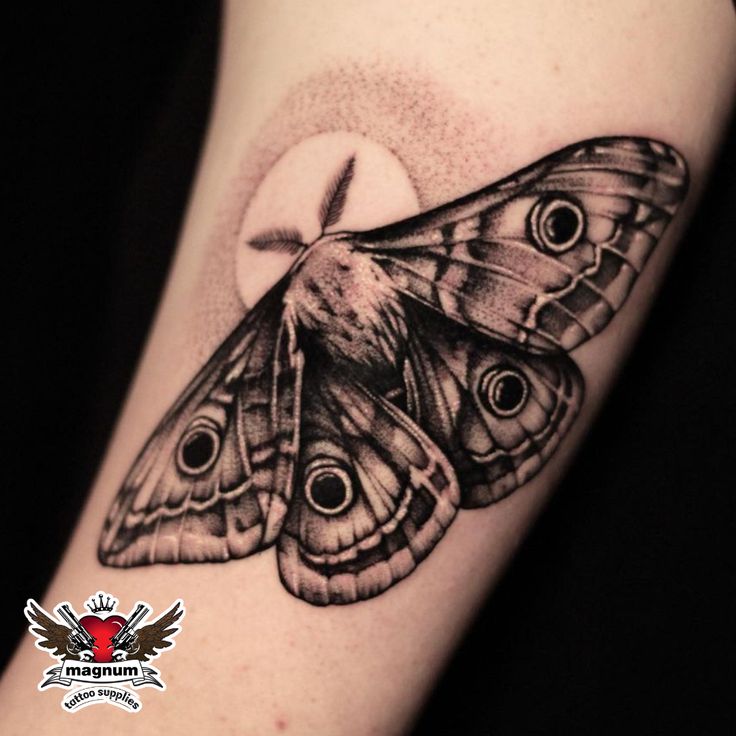 a black and white photo of a moth tattoo on the right arm, with an eyeball in the center