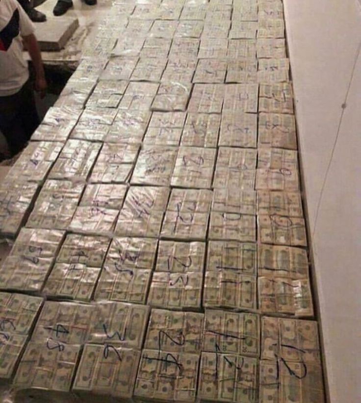 stacks of dollar bills sitting on top of a counter in a room with people standing around