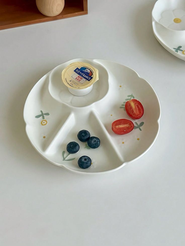 an empty plate with blueberries, tomatoes and cheese in it on a white table