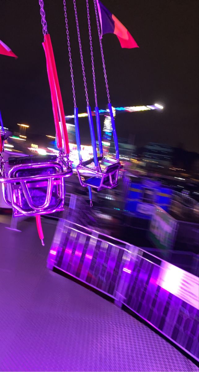 some purple and red flags hanging from the side of a boat at night with lights in the background