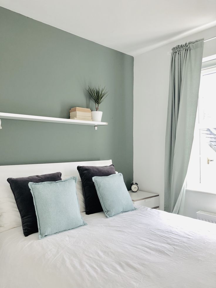 a white bed sitting in a bedroom next to a window with green drapes on the windowsill