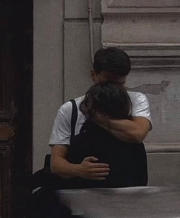 two people hugging each other in front of a building