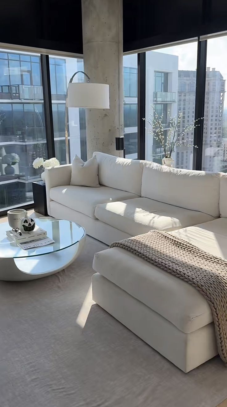 a living room filled with white furniture next to large windows and floor to ceiling windows