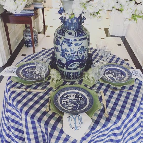 a blue and white table setting with flowers in vases on the tablecloth, plates and utensils