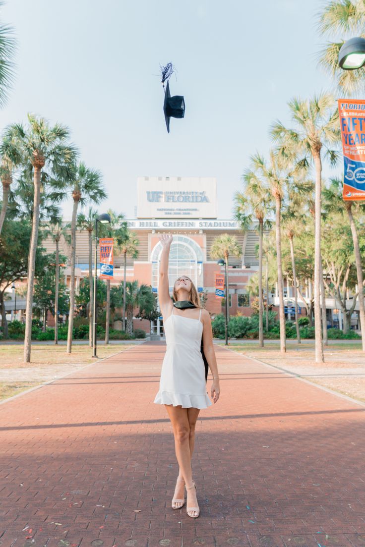 a woman in a white dress is flying a kite on a brick walkway near palm trees