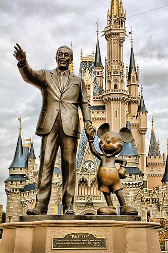 a statue of walt and mickey mouse in front of a castle