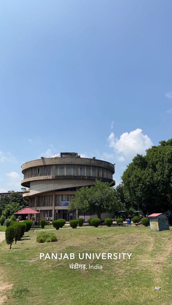 the panjab university building in india is surrounded by green grass and trees on a sunny day