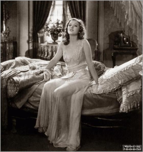 a woman sitting on top of a bed in a room with curtains and drapes