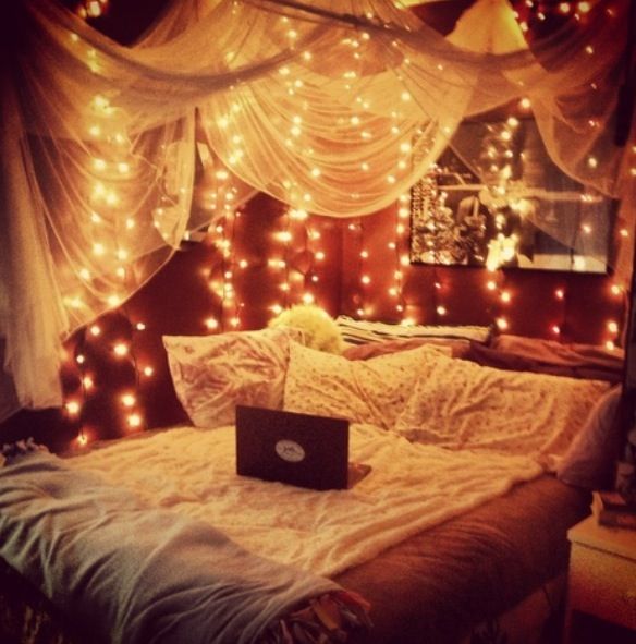 a laptop computer sitting on top of a bed covered in fairy lights and drapes