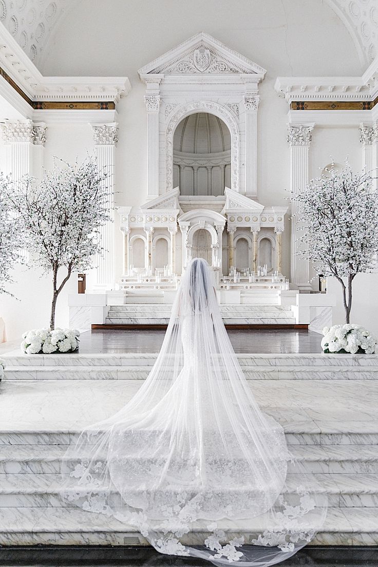 a woman in a wedding dress is standing at the alter with her veil blowing in the wind