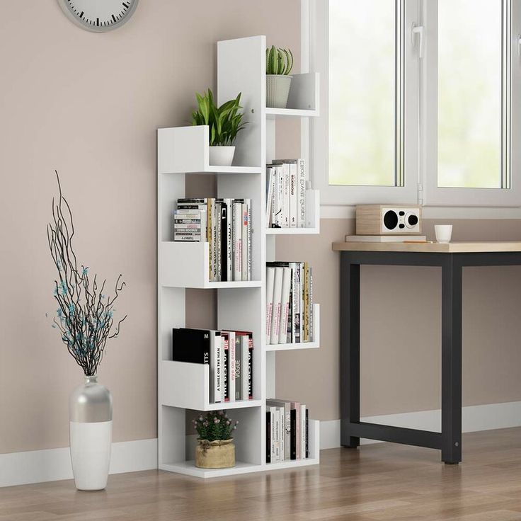 a white book shelf with books and plants on it in front of a wall clock