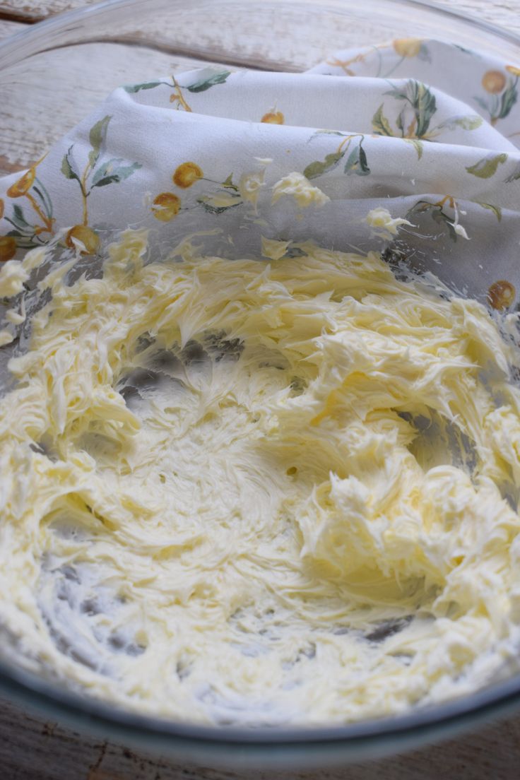 a glass bowl filled with white batter on top of a wooden table next to a napkin