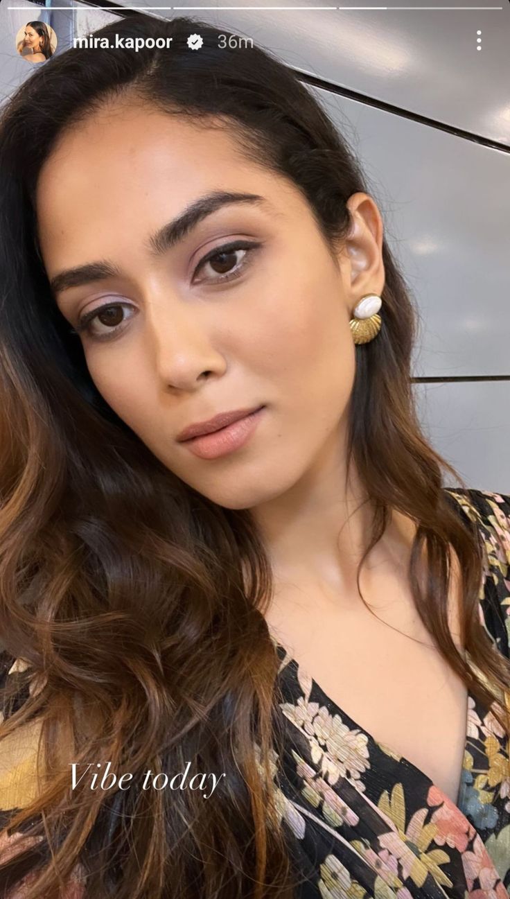 a woman with long brown hair wearing earrings and looking at the camera while standing in front of a wall