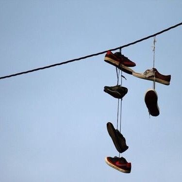 several pairs of shoes hanging on a wire with sky in the backgrouds