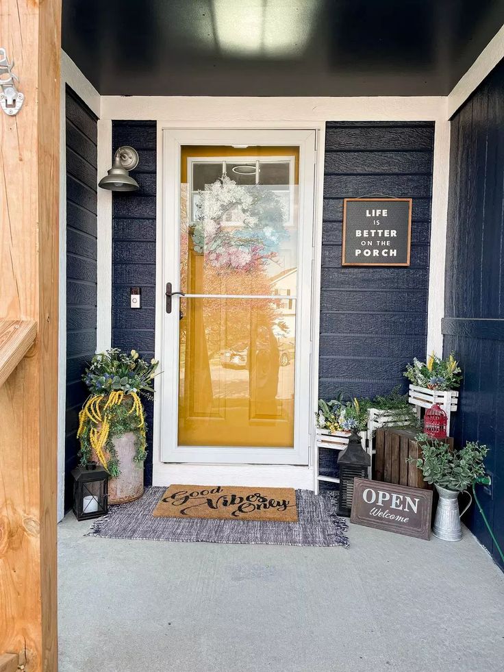 a yellow door is on the side of a blue house with two potted plants