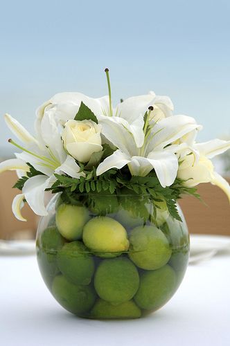 a vase filled with lots of white flowers and green apples on top of a table