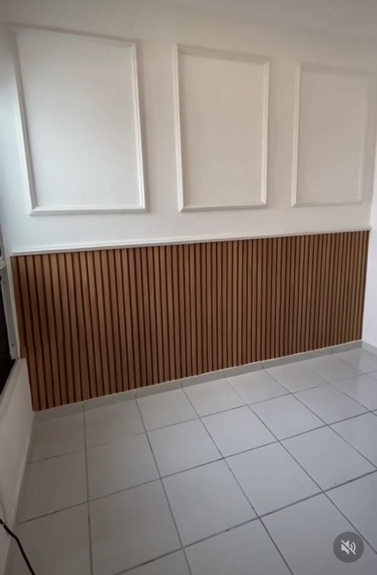 an empty room with white tile and wood paneling on the wall, in front of a window