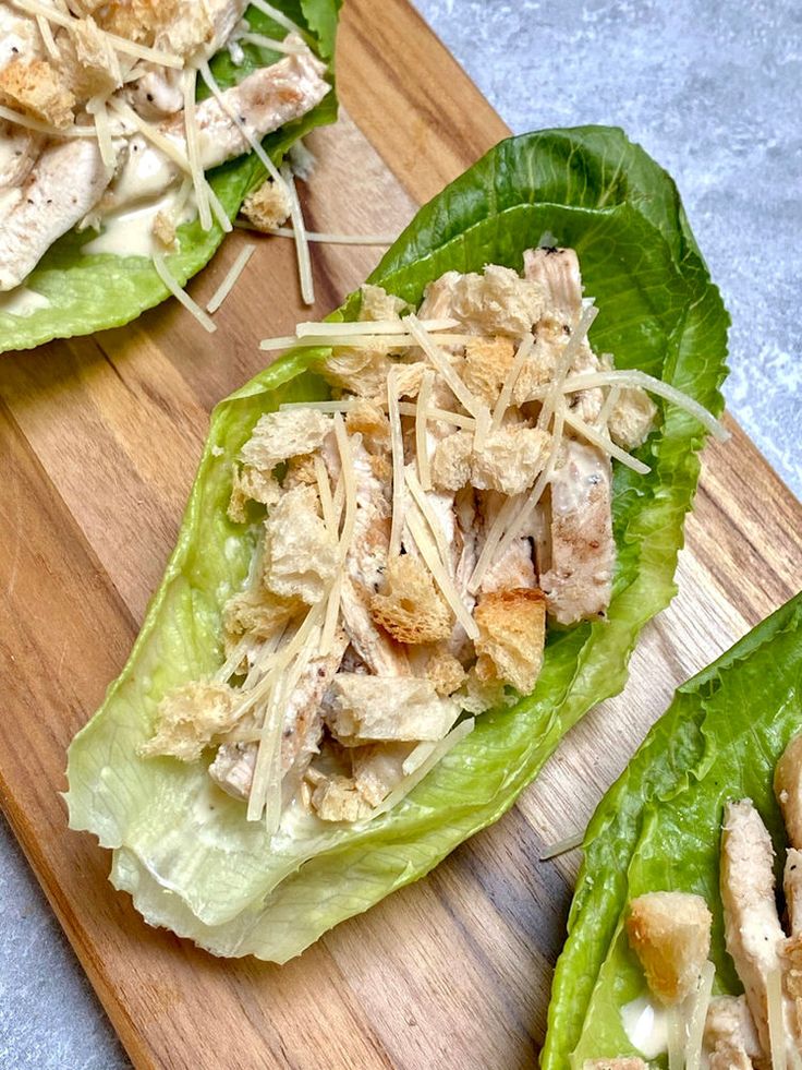 two lettuce leaves with chicken and cheese on them sitting on a cutting board