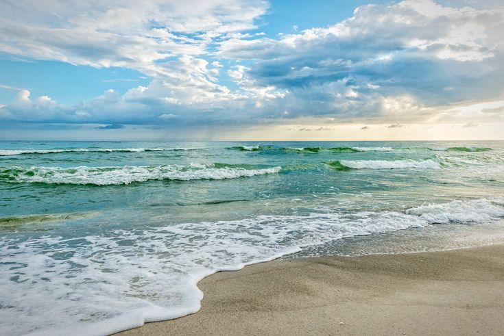 the ocean waves are rolling in to shore on a sunny day with blue sky and white clouds