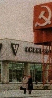 two people are walking in front of a building with a large red and white sign