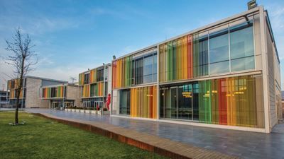 a building with multicolored glass windows on the front and side of it, sitting next to a grassy area