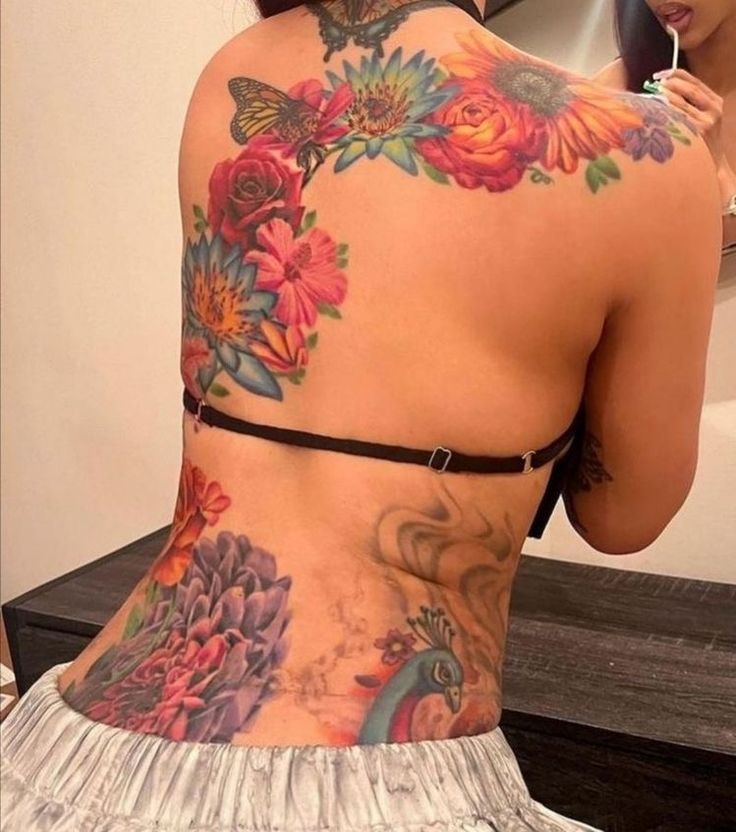 a woman with tattoos on her back is looking at herself in the mirror