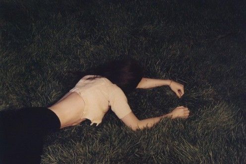 a woman laying in the grass with her head on her knees and arms behind her back