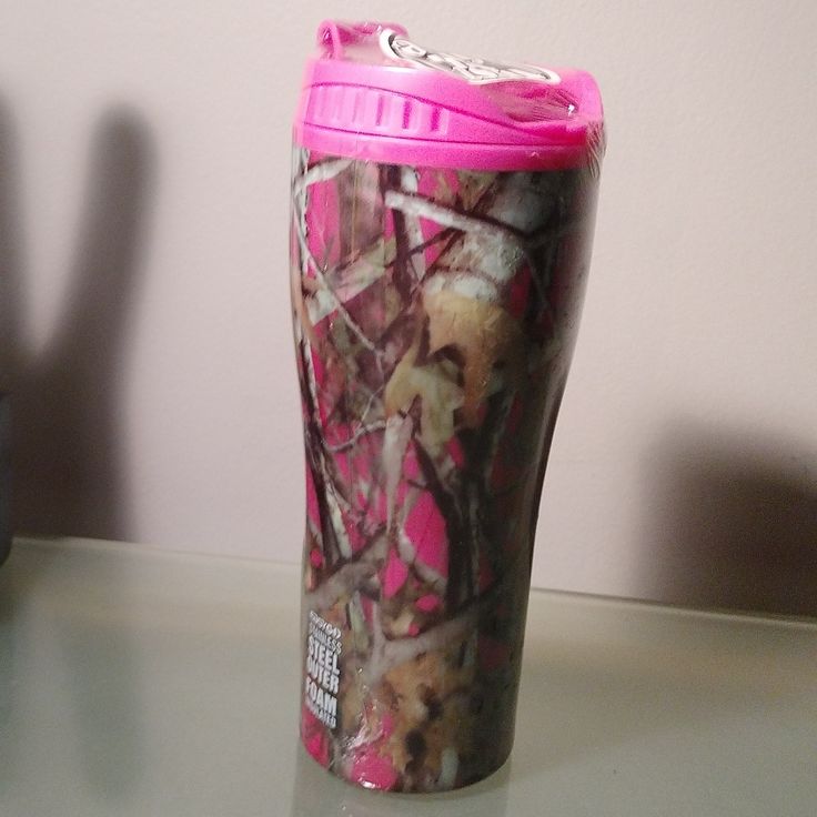 a cup with pink lid sitting on top of a table next to a black vase