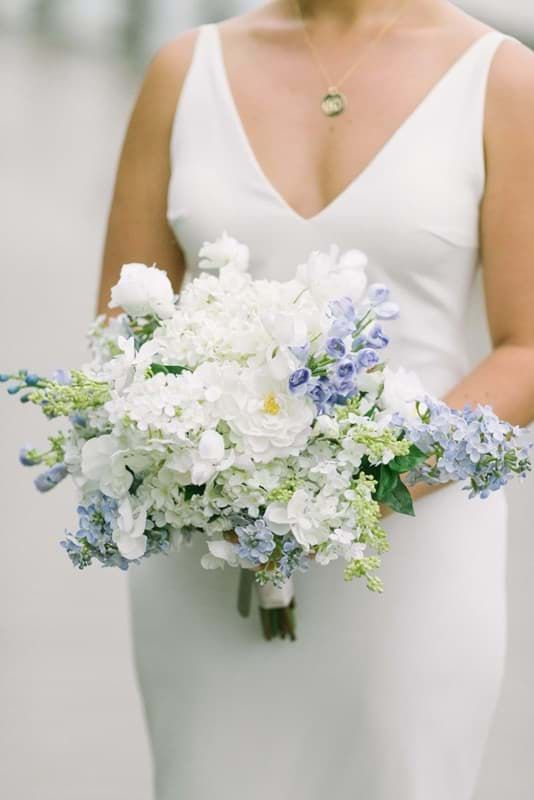 a woman in a white dress holding a bouquet of blue and white flowers on her wedding day