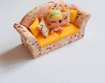 a small doll sitting on top of a yellow couch with pillows and pillow cases around it