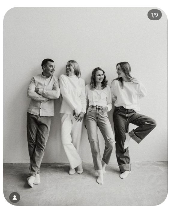 black and white photograph of four people leaning against a wall with their hands on their hipss