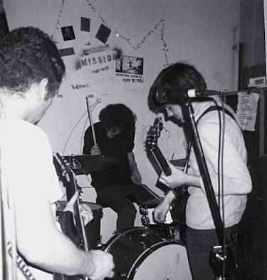 three people are playing instruments in front of a microphone and another person is singing into the mic