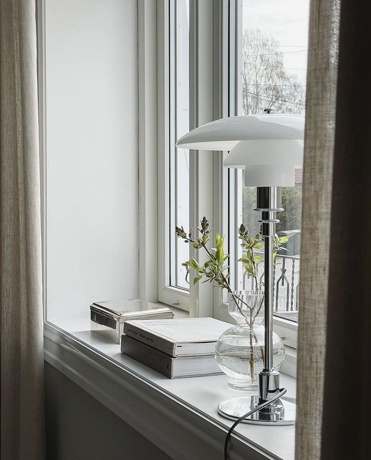 a window sill with a lamp, books and flowers on it next to a window