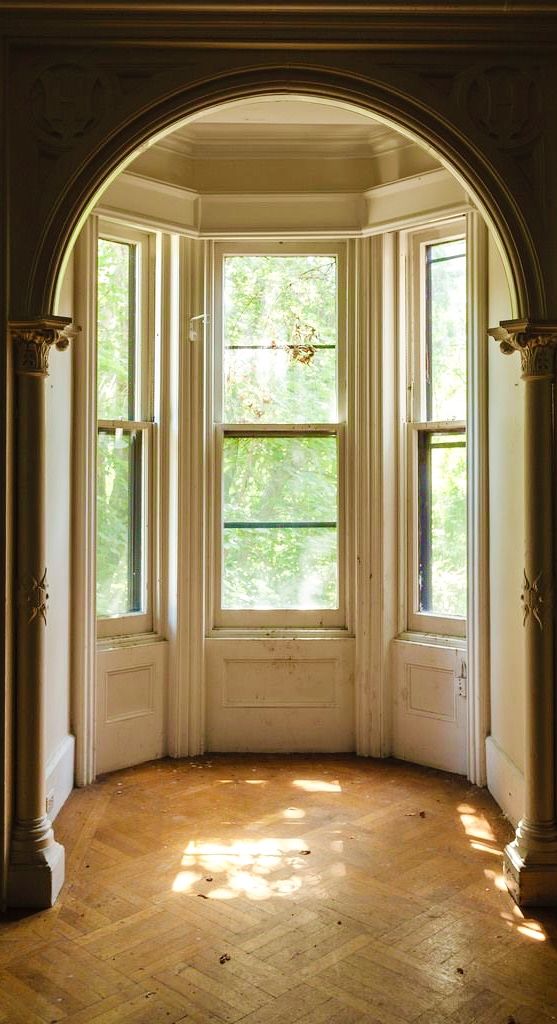 an arched window in the corner of a room with wood flooring and white walls