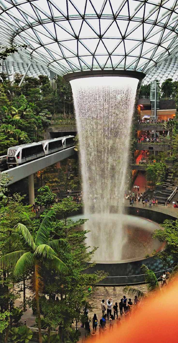 a large waterfall in the middle of a mall filled with lots of trees and people