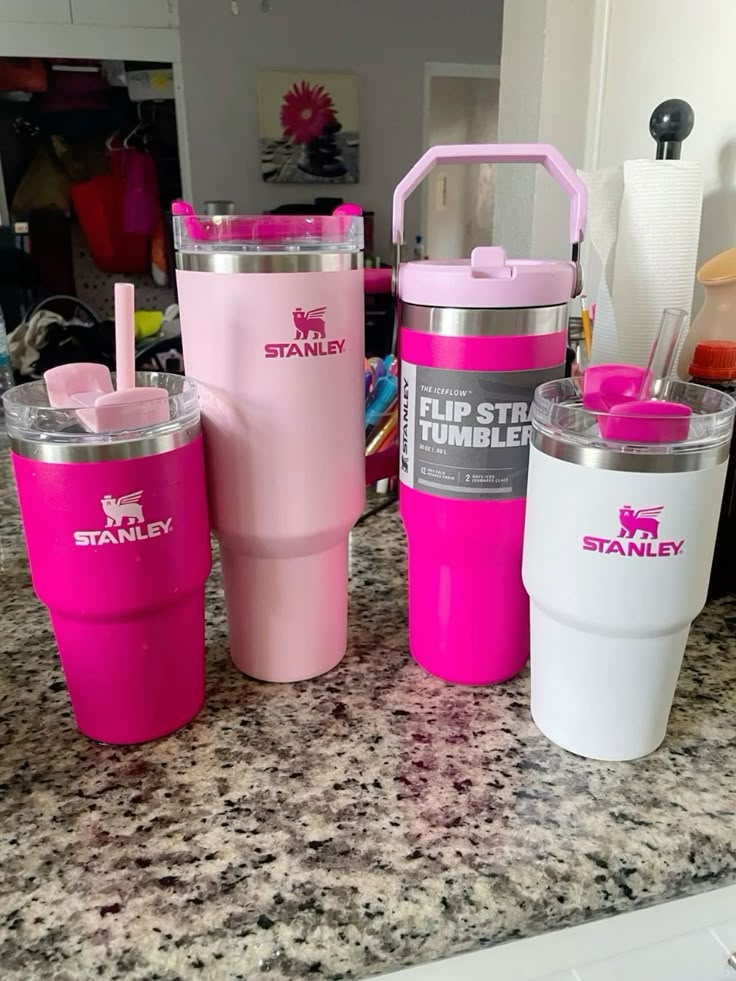 three pink tumblers sitting on top of a counter next to a cup with a straw in it