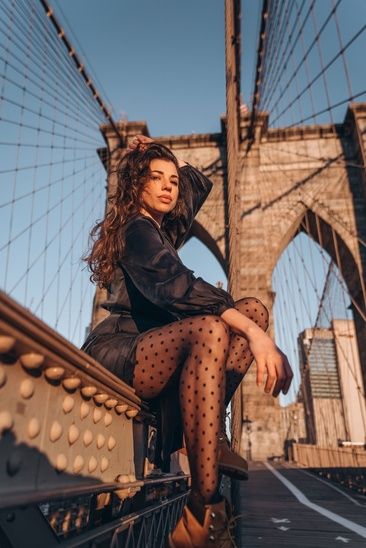 a woman sitting on top of a bridge next to the brooklyn bridge with her legs crossed