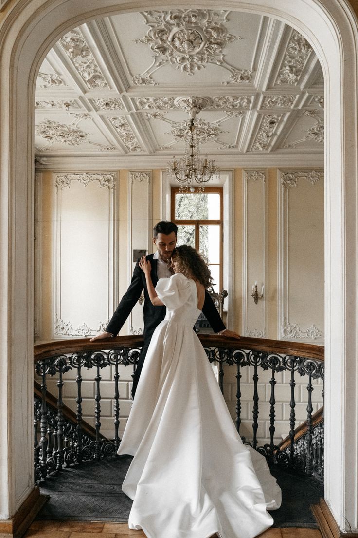 a bride and groom are standing on the stairs in an ornate building with chandeliers