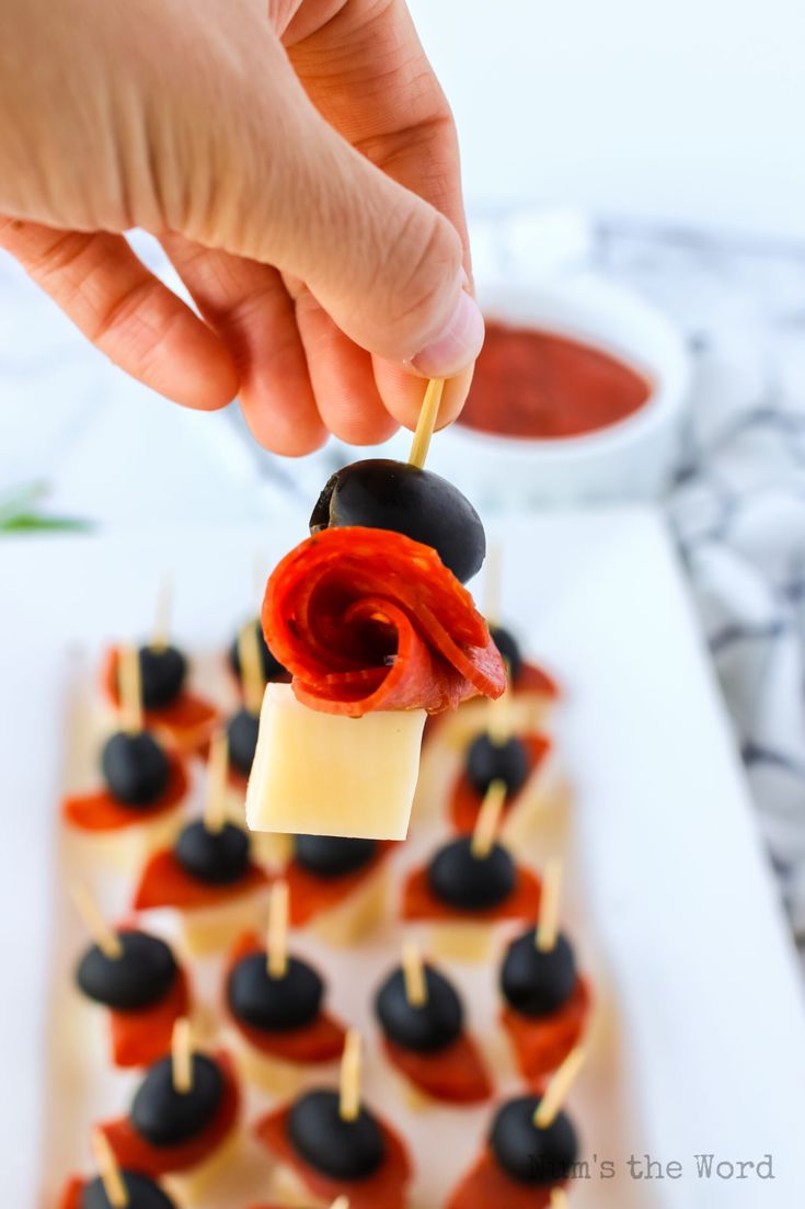 a person is picking up some food from a plate with black olives on it