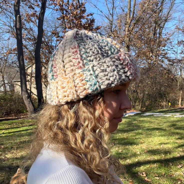 a woman wearing a multicolored knitted hat in the park with trees and grass behind her