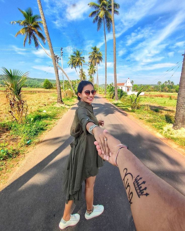 a woman holding the hand of a man on a road with palm trees in the background