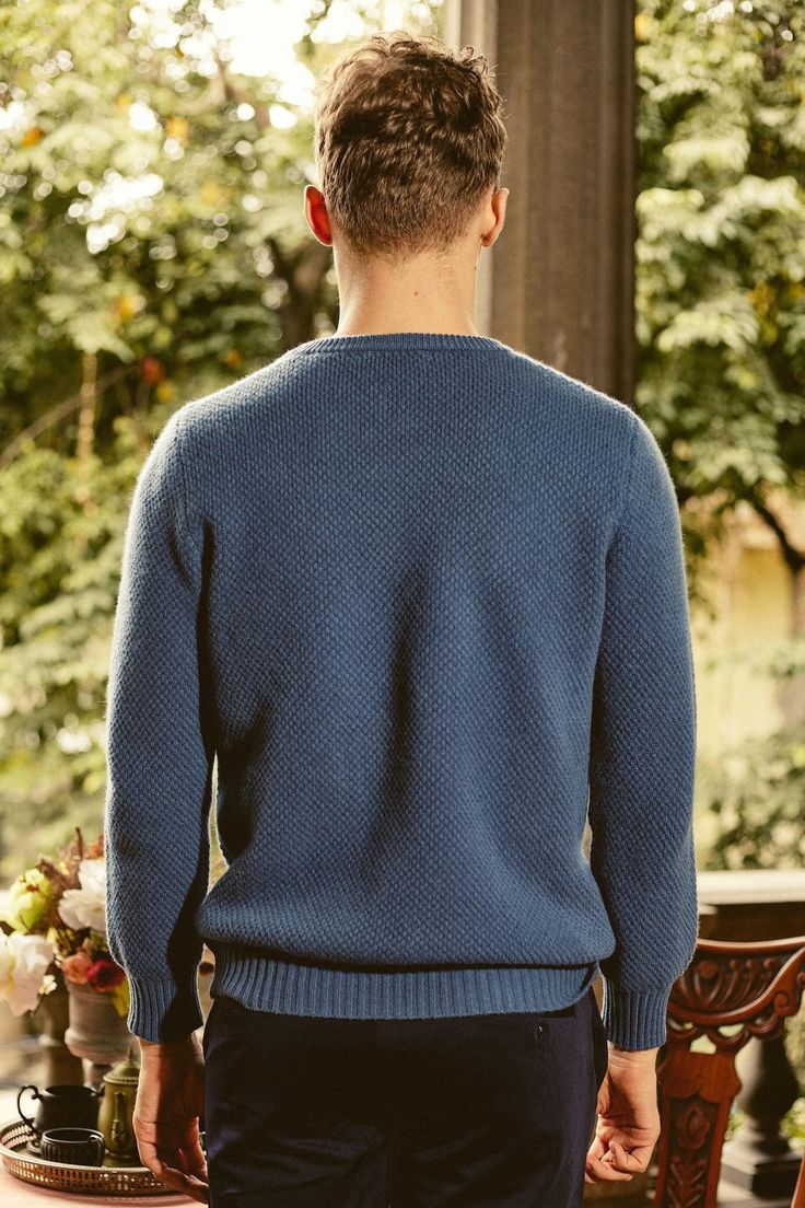 a man standing in front of a table wearing a blue sweater and black pants with his back turned to the camera