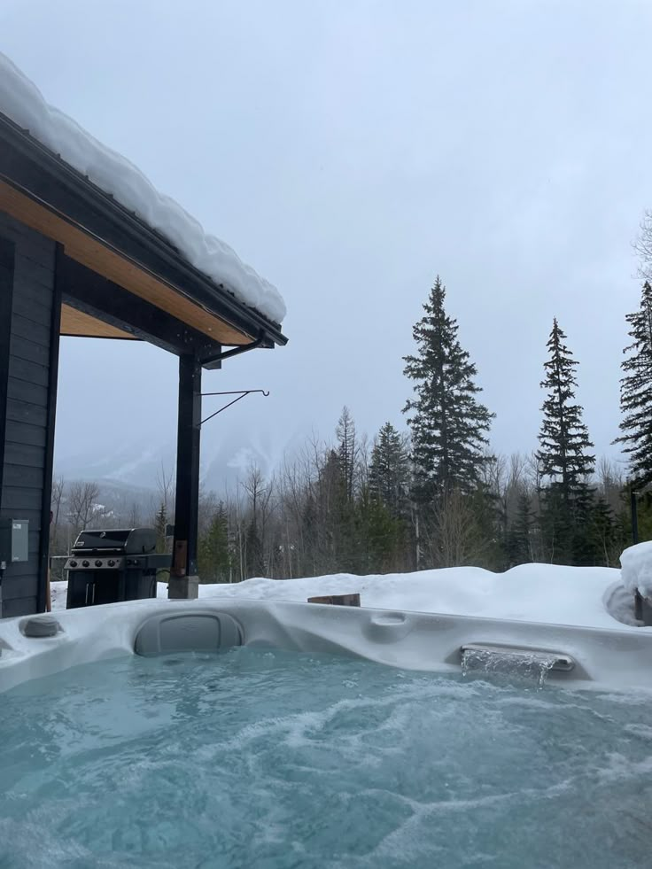 an outdoor hot tub covered in snow next to a building with trees on the other side