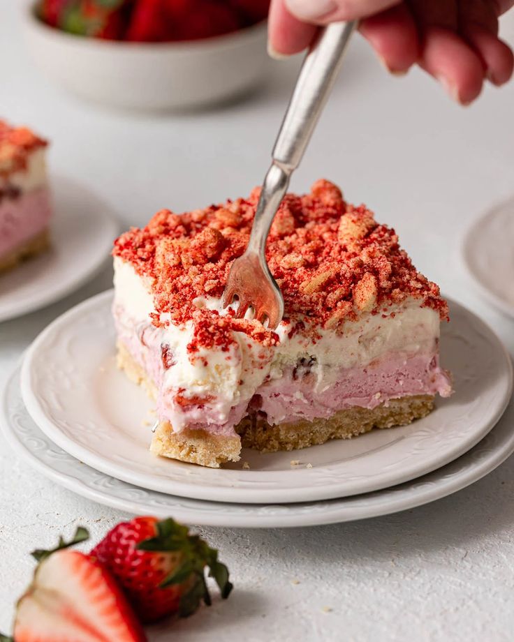 someone cutting into a piece of cake on a plate with strawberries in the background