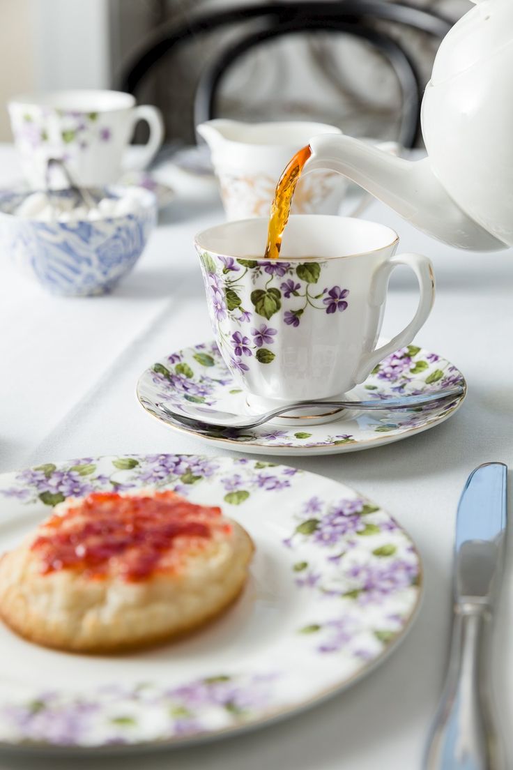 tea being poured into a cup and saucer on a white table with purple flowers