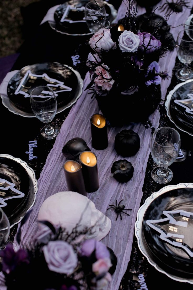 the table is set with black and white plates, silverware, candles and flowers