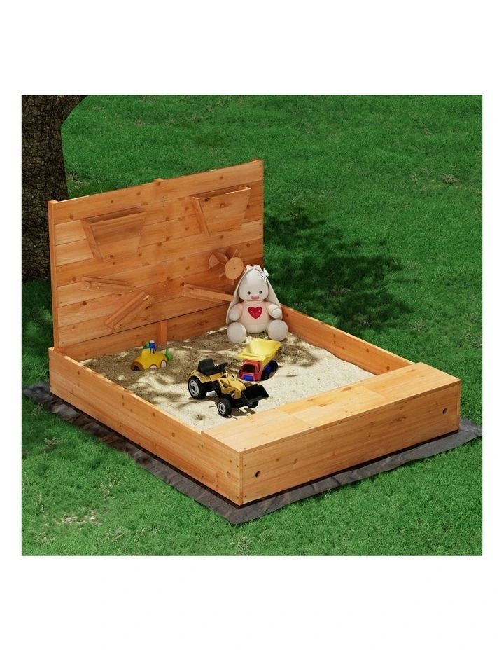 a wooden bed with sand and toys in it on the grass next to a tree