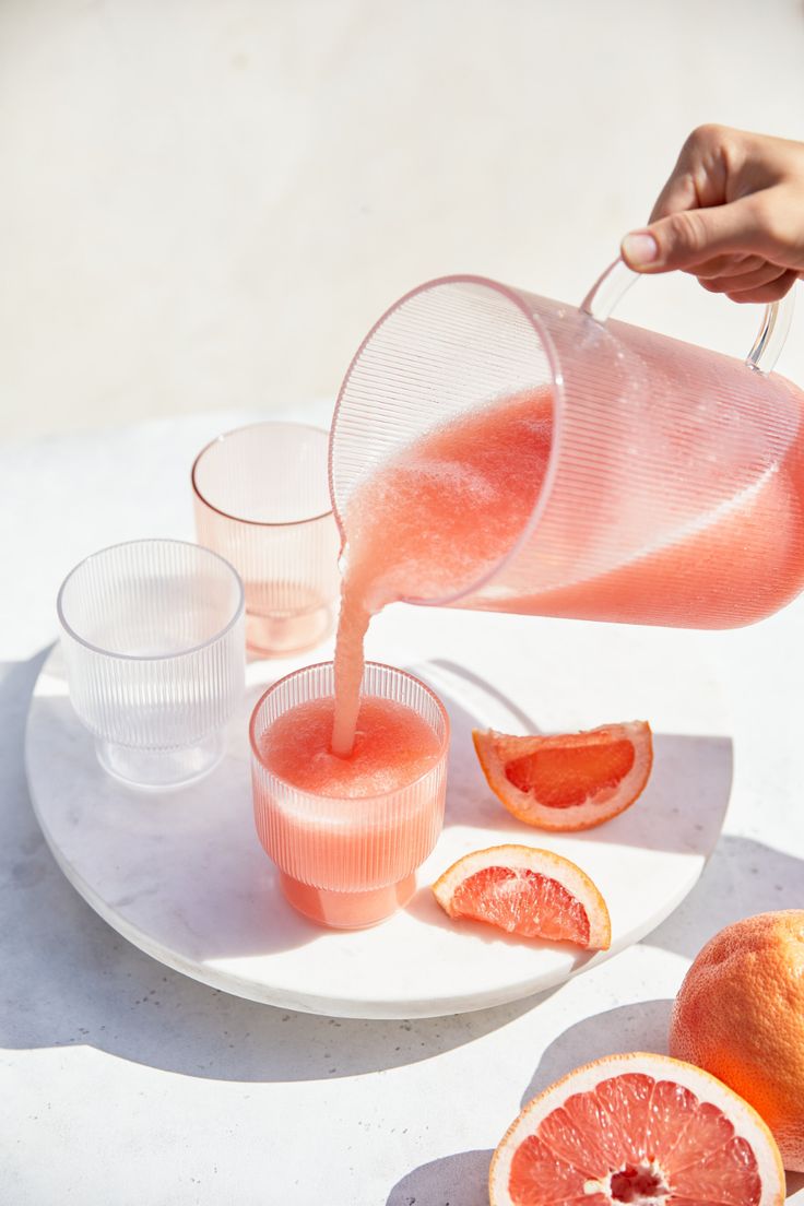 a person pours orange juice into cups on a plate with grapefruit slices