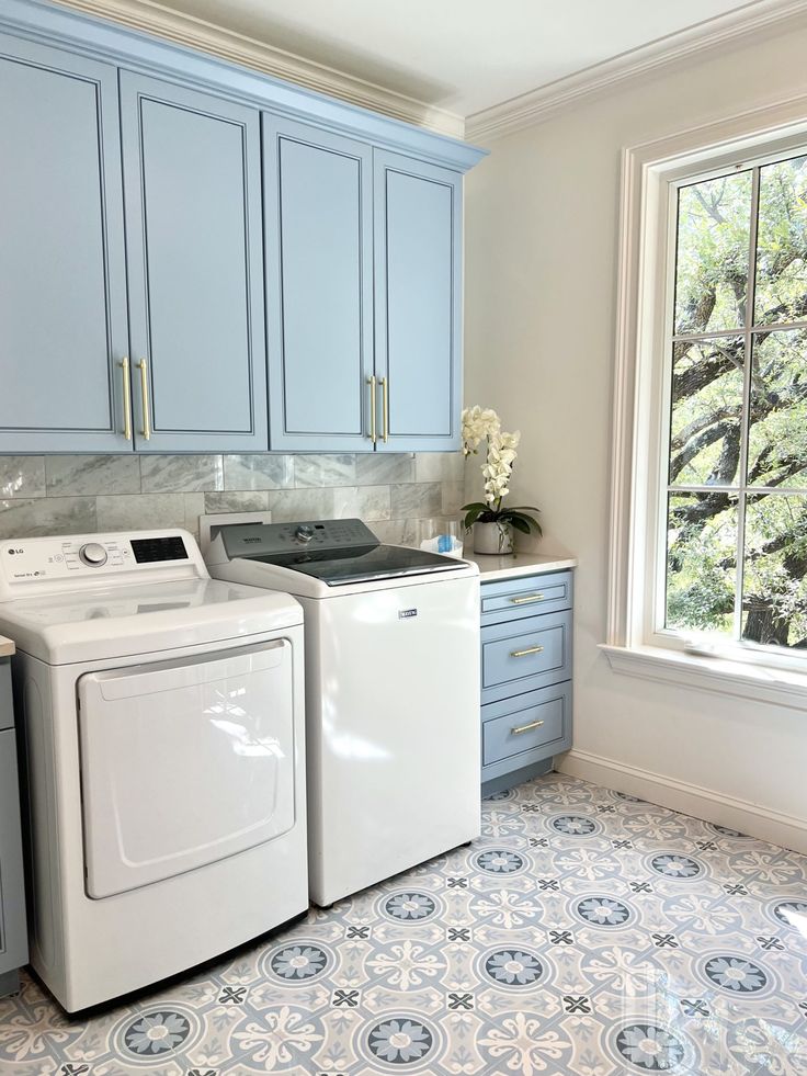 a washer and dryer sitting in a kitchen next to a window with blue cabinets