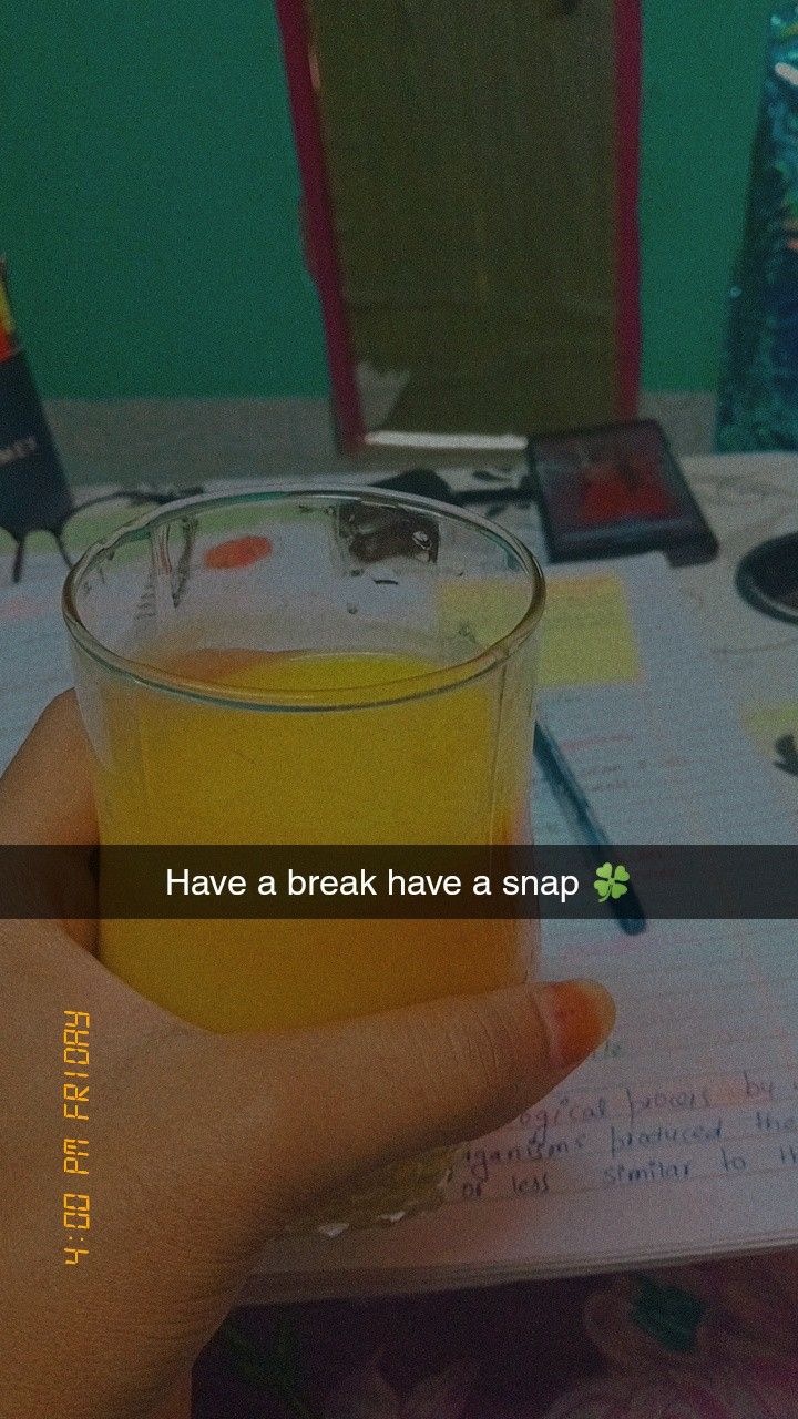 a person holding a glass filled with orange juice on top of a table next to a book